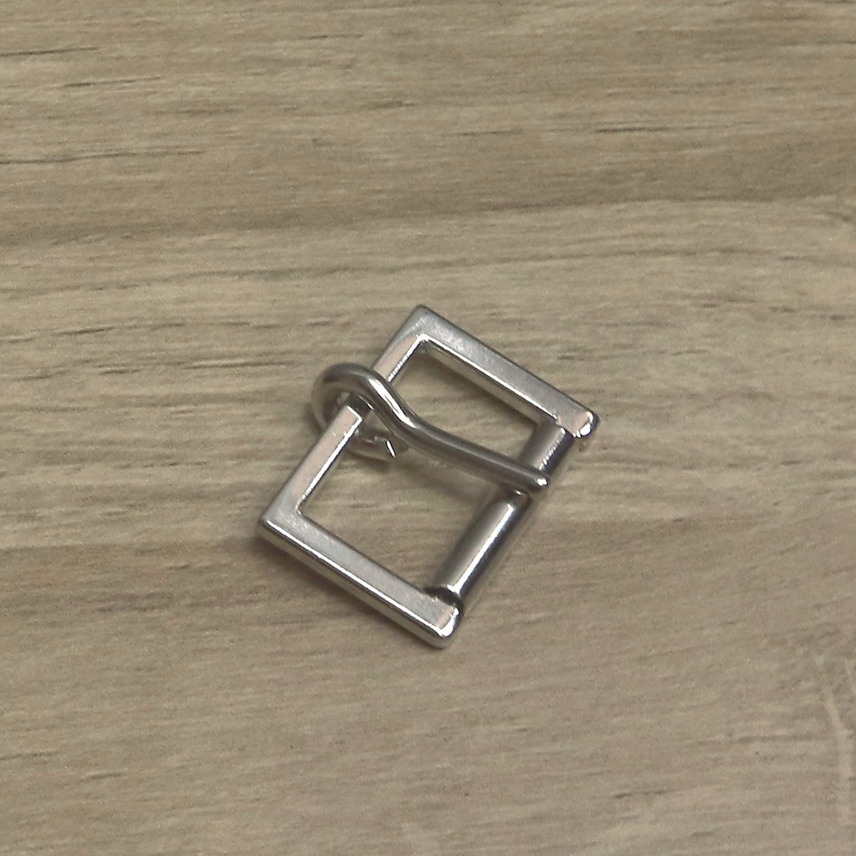 Nickel-plated cast buckle with a squared frame, at an angle with the pin resting on the roller