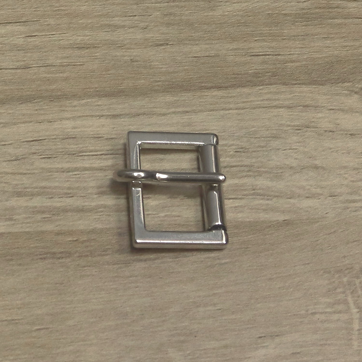 Nickel-plated cast buckle from above, pin lying across the frame onto the roller