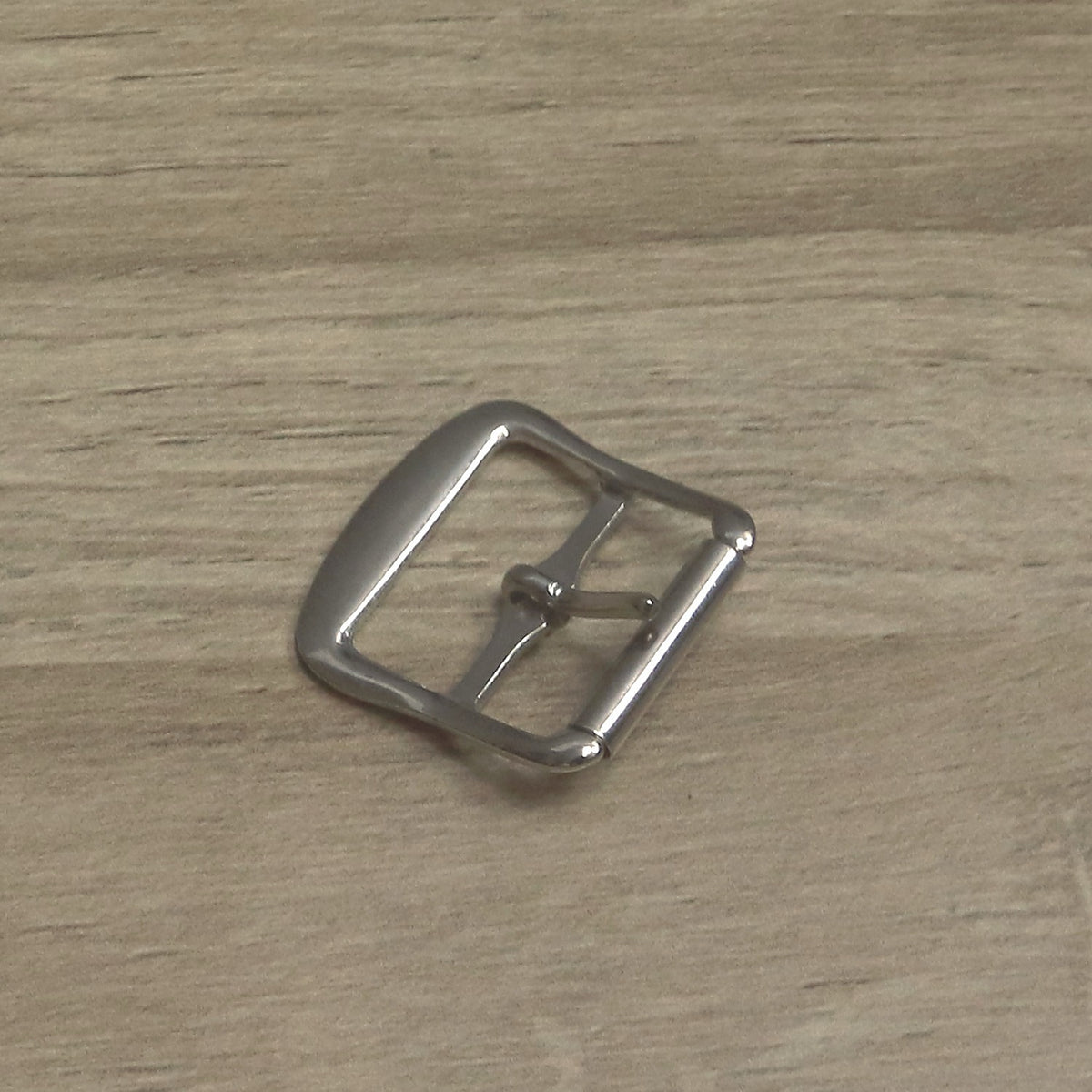 Nickel-plated roller buckle for a 25mm strap, angled to show the curve of the frame and the pin resting on the roller