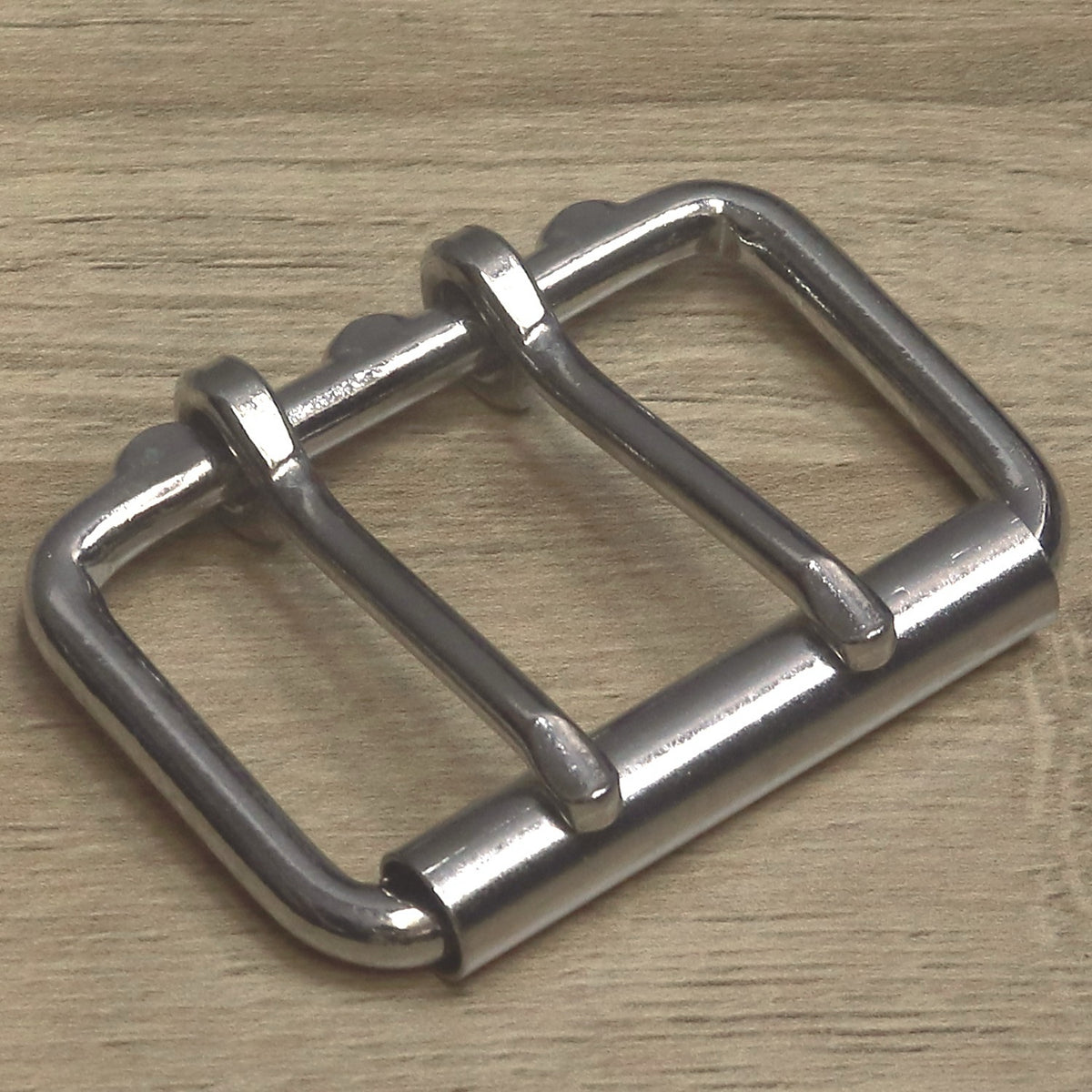 Nickel plated double prong roller buckle, angled view showing the roller and both pins