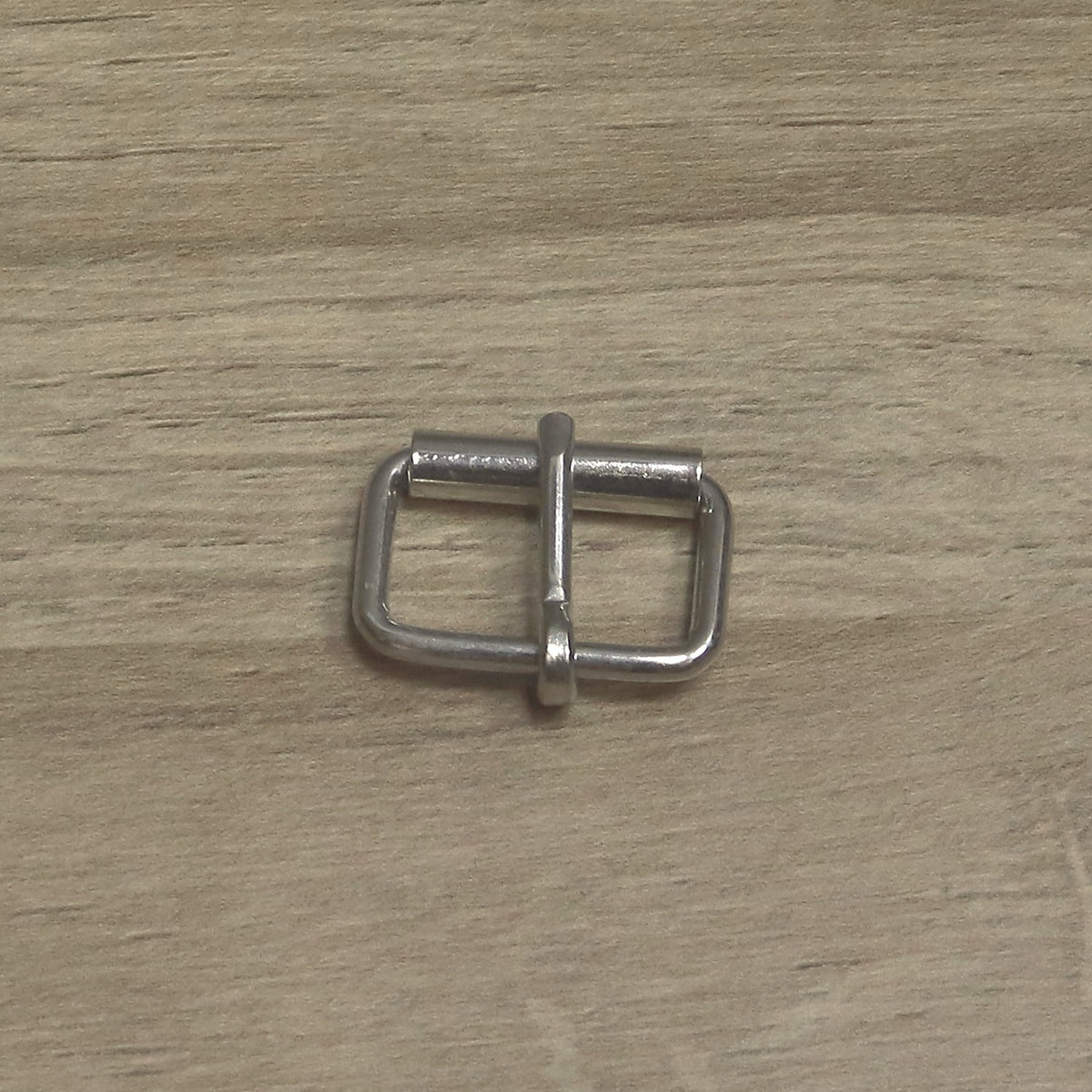 Nickel-plated 25mm wire roller buckle laid sideways, roller along the top and pin pointing up across it