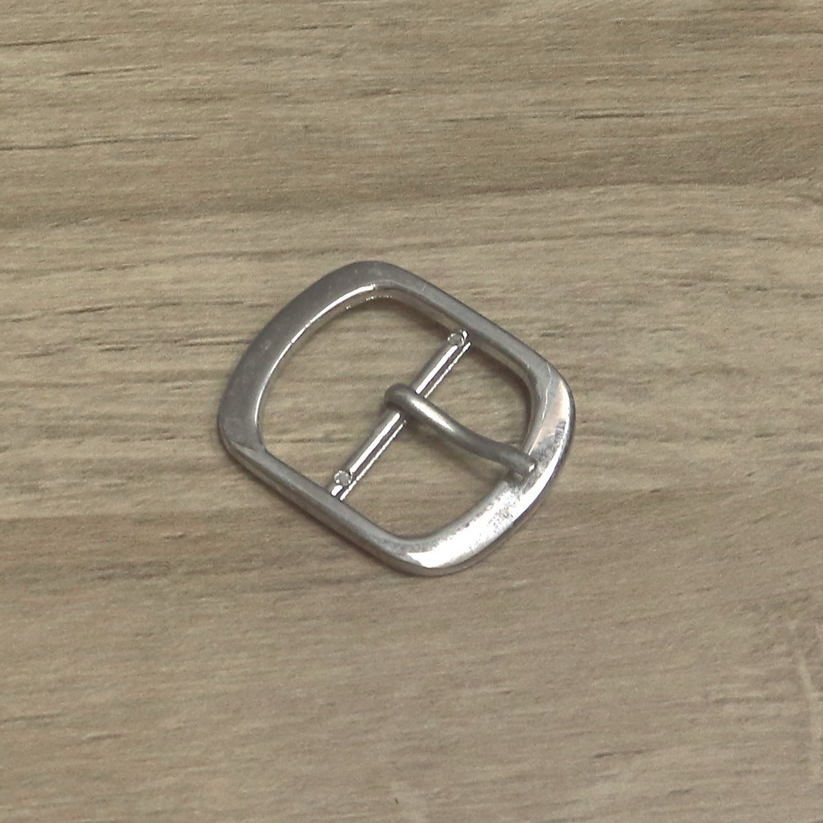 Nickel-plated oval buckle for a 25mm strap, angled with the pin resting on the front of the frame