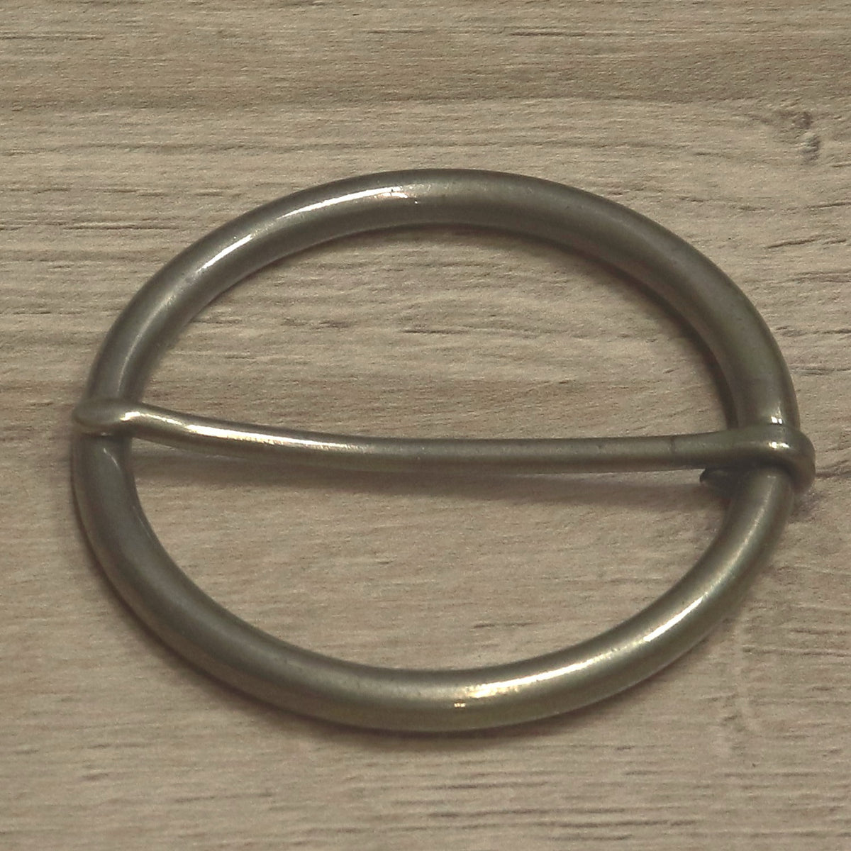 Antique brass round buckle from above, pin lying across the ring