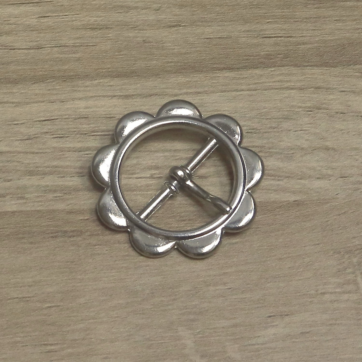 Nickel-plated round buckle with scalloped petals around the rim, the pin resting across the ring from its centre bar