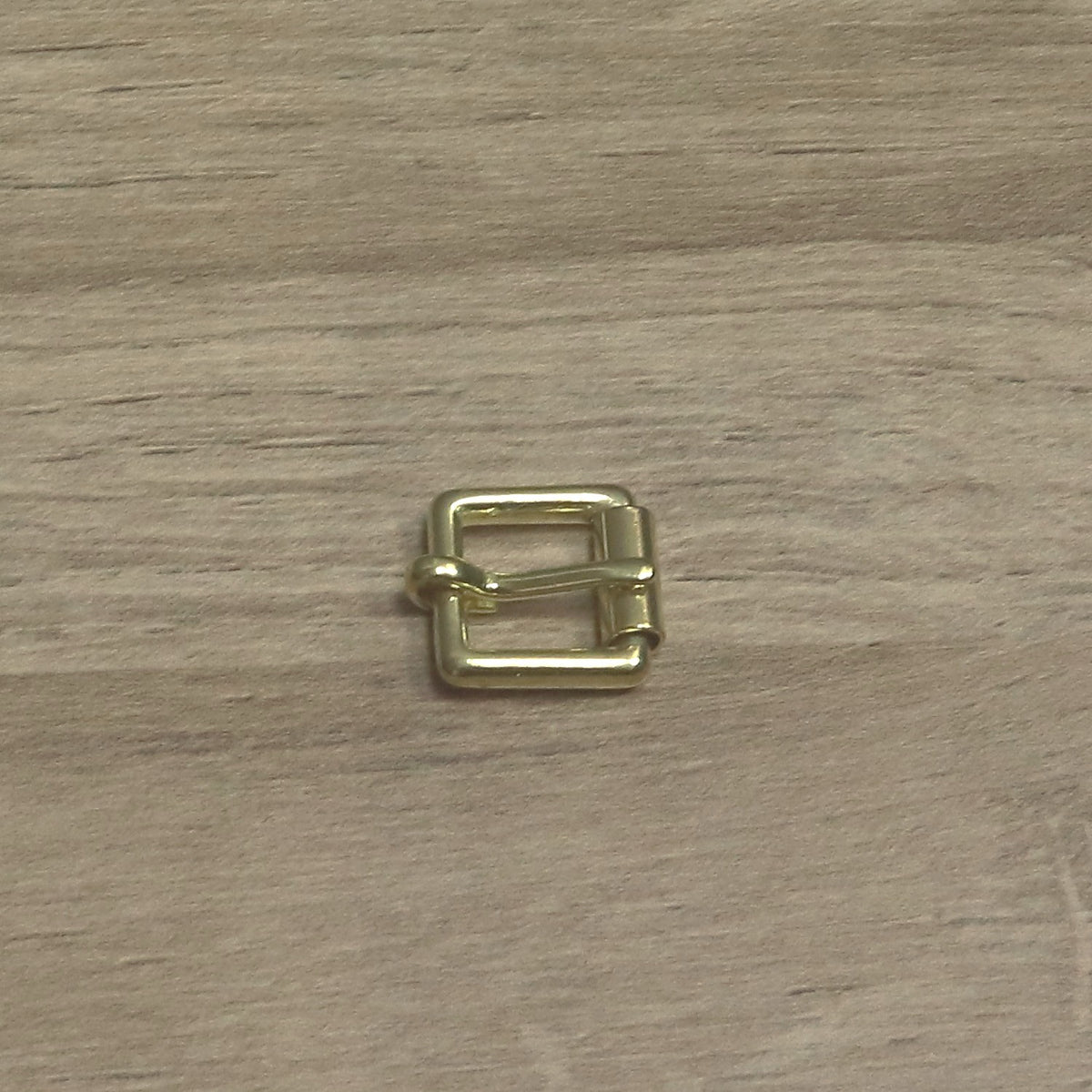 Small brass buckle from above, pin looped round the back bar and resting on the roller