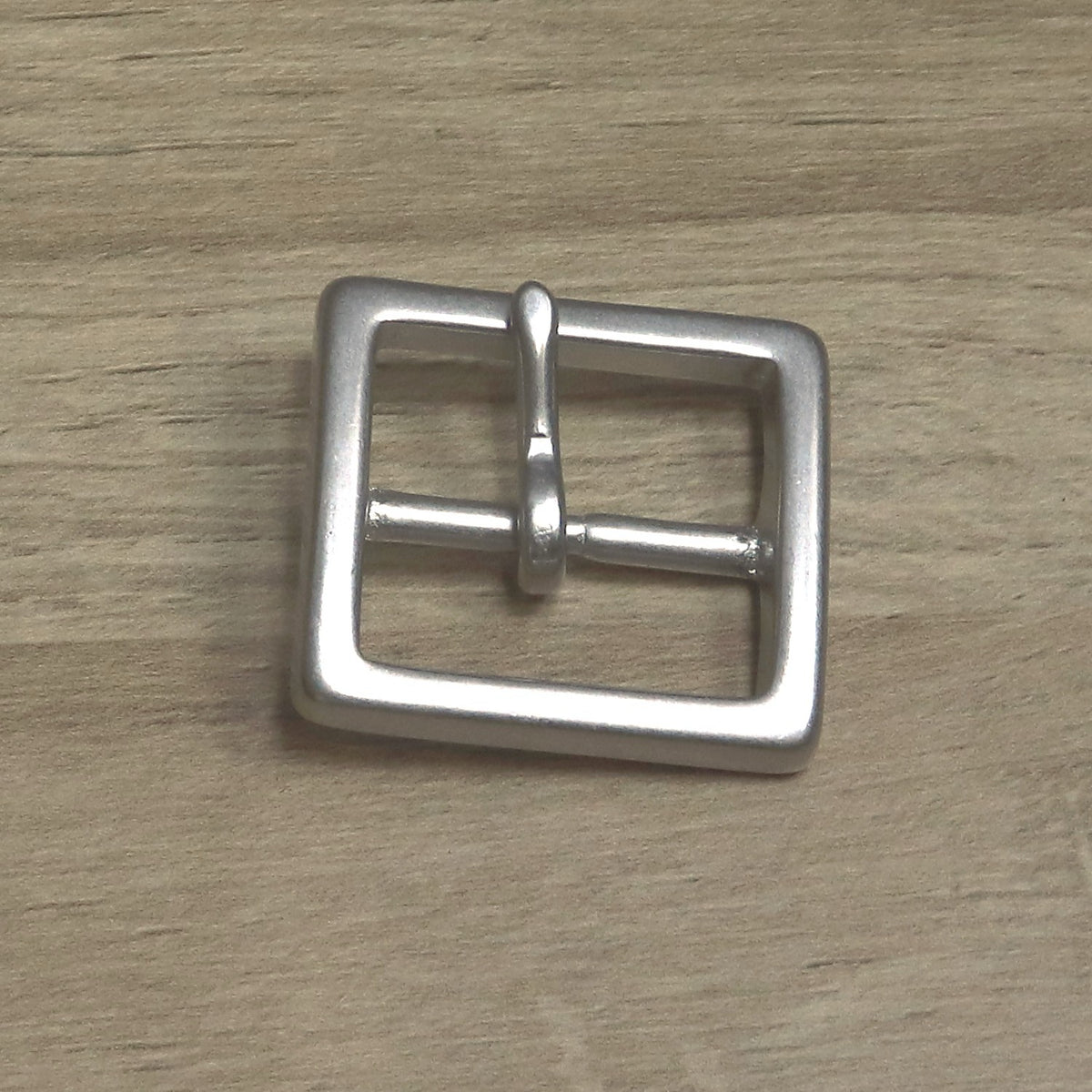 Square cast buckle from above with the pin pointing up across the frame